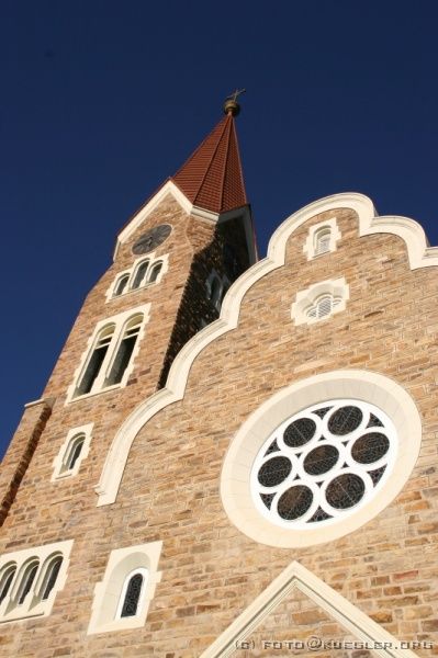 IMG_5189 <p><b>Die Christuskirche in Windhoek</b></p>
<br>
<div align=left>
<p><b>17. und 18. Oktober 2008: Abflug, Ankunft in Windhoek.</b></p>

<P>Um kurz vor 17.00 Uhr am 17.Oktober holt uns Kathrins Schwester wie verabredet mit unseren gepackten Rucksäcken und Taschen ab und fährt uns zum Bahnhof, wo wir den ausnahmsweise mal pünktlichen ICE um 17.17 Uhr nach Frankfurt nehmen. Laut unserem Reiseanbieter Djoser sollen wir uns schon drei statt zwei Stunden vor Abflug zum Einchecken einfinden, was zur Folge hat, dass wir mit -zig anderen in einer Warteschlange in "Parkposition" stehen, bevor der Schalter der Air Namibia überhaupt öffnet !</P>

<P>Gut! Nach langem Beine-in-den-Bauch-stehen schaffen wir auch das irgendwann. Am Schalter guckt die Flughafenangestellte etwas gekniffen, denn nicht KUEGLER STEFAN sondern KUEGLER R. steht auf der Passagierliste. Zum Glück lässt sie sich überzeugen, uns beide mitzunehmen.</P>

<P>Bald nach dem Start der Maschine um 22.45 Uhr bekommen wir dann einen Mitternachtssnack, und als die Kabinenlichter ausgehen, versuchen wir mehr oder weniger erfolgreich, etwas Schlaf zu finden. Beim Blick aus den Flugzeugfenstern blitzt und gewittert es in allen sichtbaren Richtungen. Wir sind zu diesem Zeitpunkt bereits über dem afrikanischen Kontinent.</P>

<P>Völlig gerädert hocken wir dann um 6.30 Uhr vor unserem Frühstück und mehr als eine Tasse Kaffee bekommen wir nicht hinunter.</P>

<P>Um 8.10 Uhr, eine halbe Stunde vor der geplanten Zeit, landen wir sicher auf dem International Airport, dem Flughafen von Windhoek, auf dem an diesem Tag die erstaunliche Anzahl von 12 Flugzeugen landen wird. Leider erwartet uns hier eine langwierige Passkontrolle, soviel zum Zeitvorsprung...</P>

<P>In der winzigen Ankunftshalle treffen wir auf Konrad, unseren Reisebegleiter, sowie auf Eddie, unseren Koch, und Robson, unseren Fahrer. Damit kann unsere gemeinsame Zeit mit insgesamt 23 Personen in einem Safaritruck losgehen.</P>
</div>